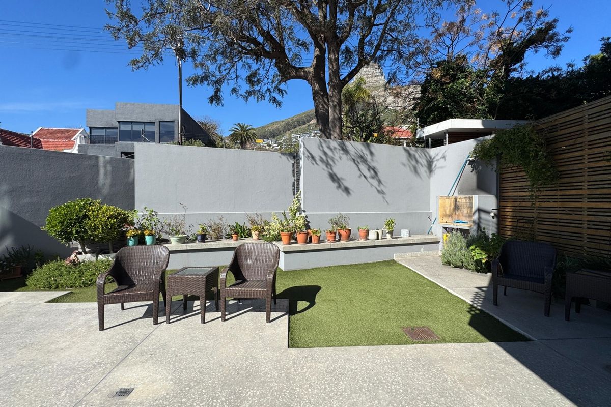 A well-maintained rear courtyard featuring a concrete patio, artificial lawn, built-in braai, and a timber privacy screen.