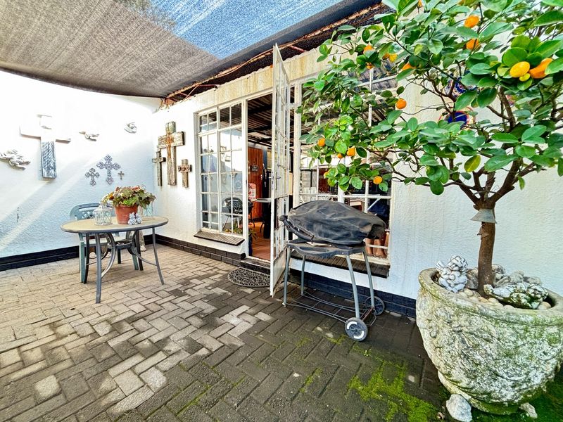 A paved outdoor patio area featuring a shade cloth covering and direct access to the interior through classic french doors.