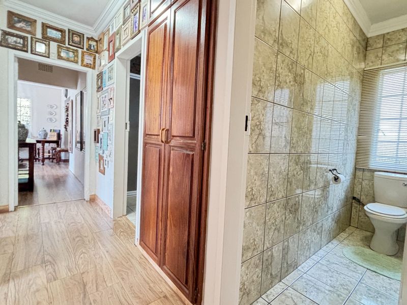 A hallway featuring wood-look flooring, built-in storage cabinetry, and an adjacent tiled bathroom area with a toilet and window blinds.