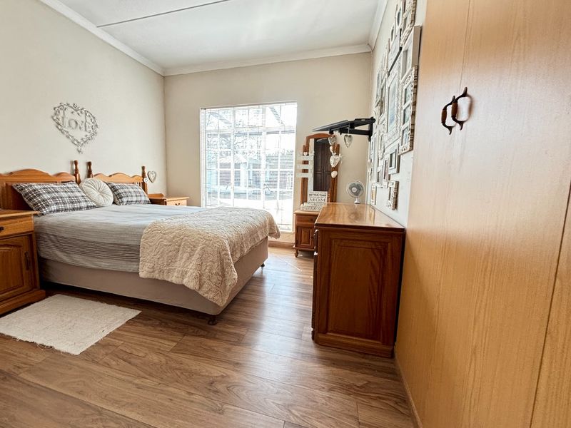 A well-maintained bedroom featuring laminate flooring, a large window with blinds, and a built-in wardrobe.
