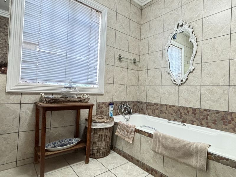 A bathroom featuring a built-in bathtub with decorative stone-accented tiling, neutral floor tiles, and a window with blinds.
