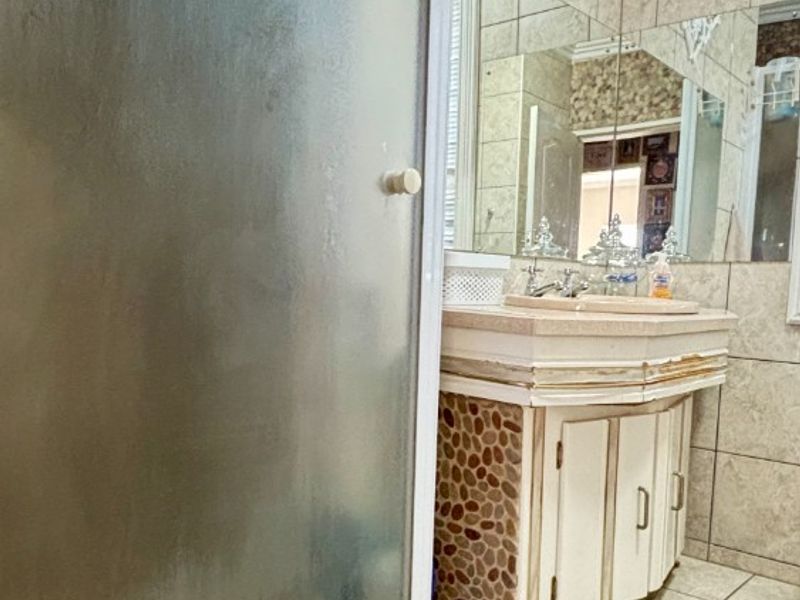 Bathroom featuring a shower enclosure, tiled surfaces, and a vanity unit with a basin. The vanity cabinet shows signs of wear and finish deterioration.