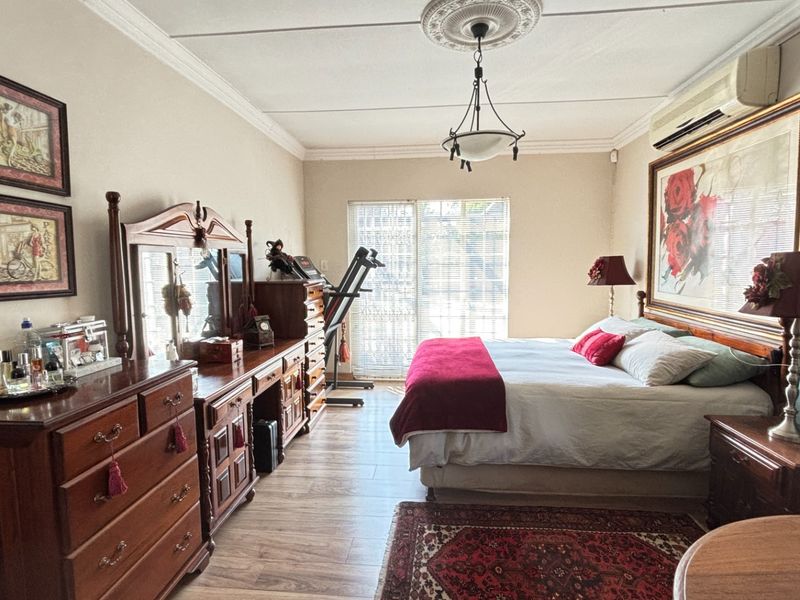 Spacious bedroom featuring laminate flooring, decorative ceiling rose with coving, and a split-system air conditioner, with direct access to the outdoors via sliding doors.