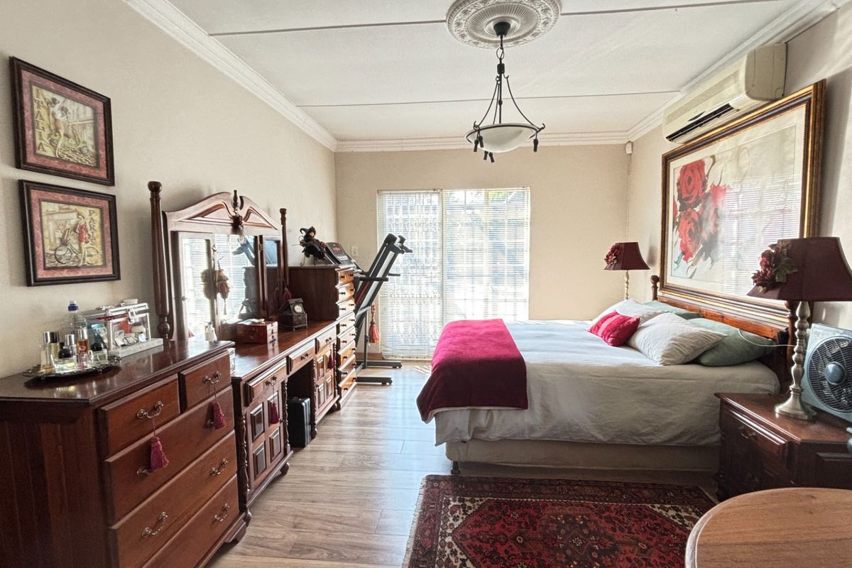 Spacious bedroom featuring laminate flooring, decorative ceiling rose with coving, and a split-system air conditioner, with direct access to the outdoors via sliding doors.
