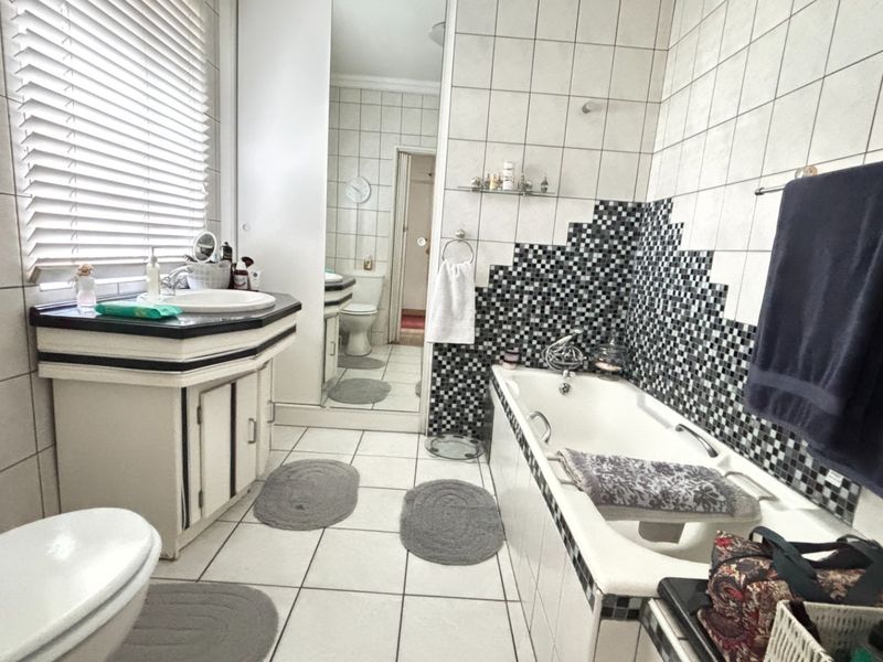 A functional bathroom featuring a built-in vanity, bathtub with tiled surround, and neutral wall tiling with a decorative mosaic accent.