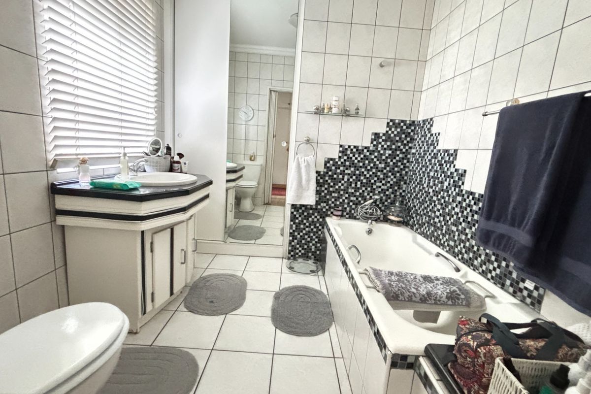 A functional bathroom featuring a built-in vanity, bathtub with tiled surround, and neutral wall tiling with a decorative mosaic accent.