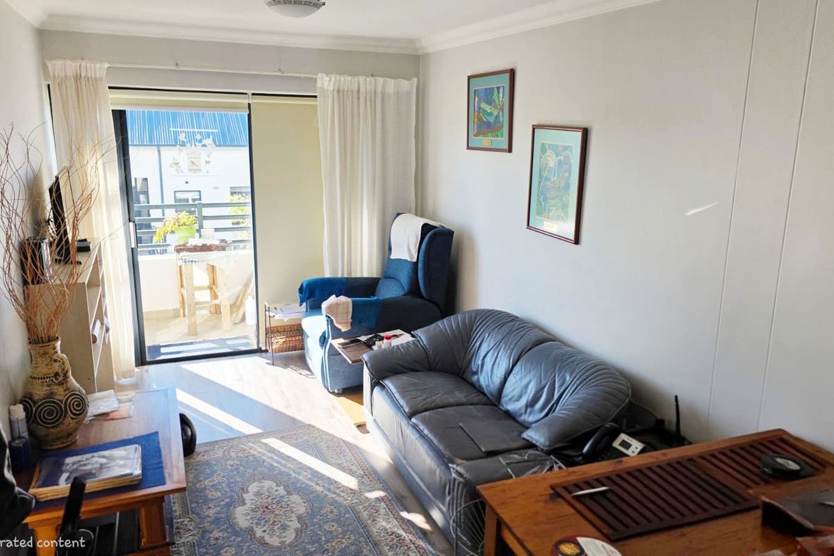 A bright living room featuring laminate flooring, coving, and a sliding glass door providing direct access to an outdoor balcony area.
