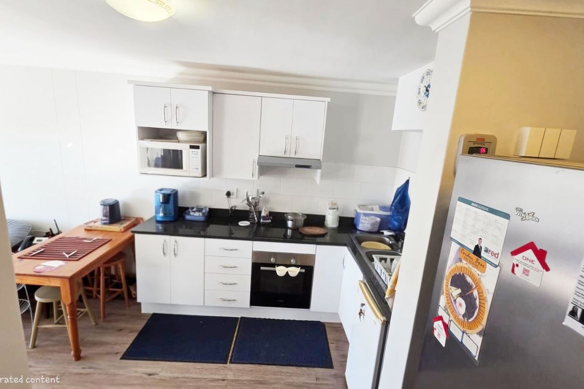 A functional kitchen featuring white cabinetry, dark stone countertops, built-in oven, extractor fan, and integrated microwave, with adjacent dining space.