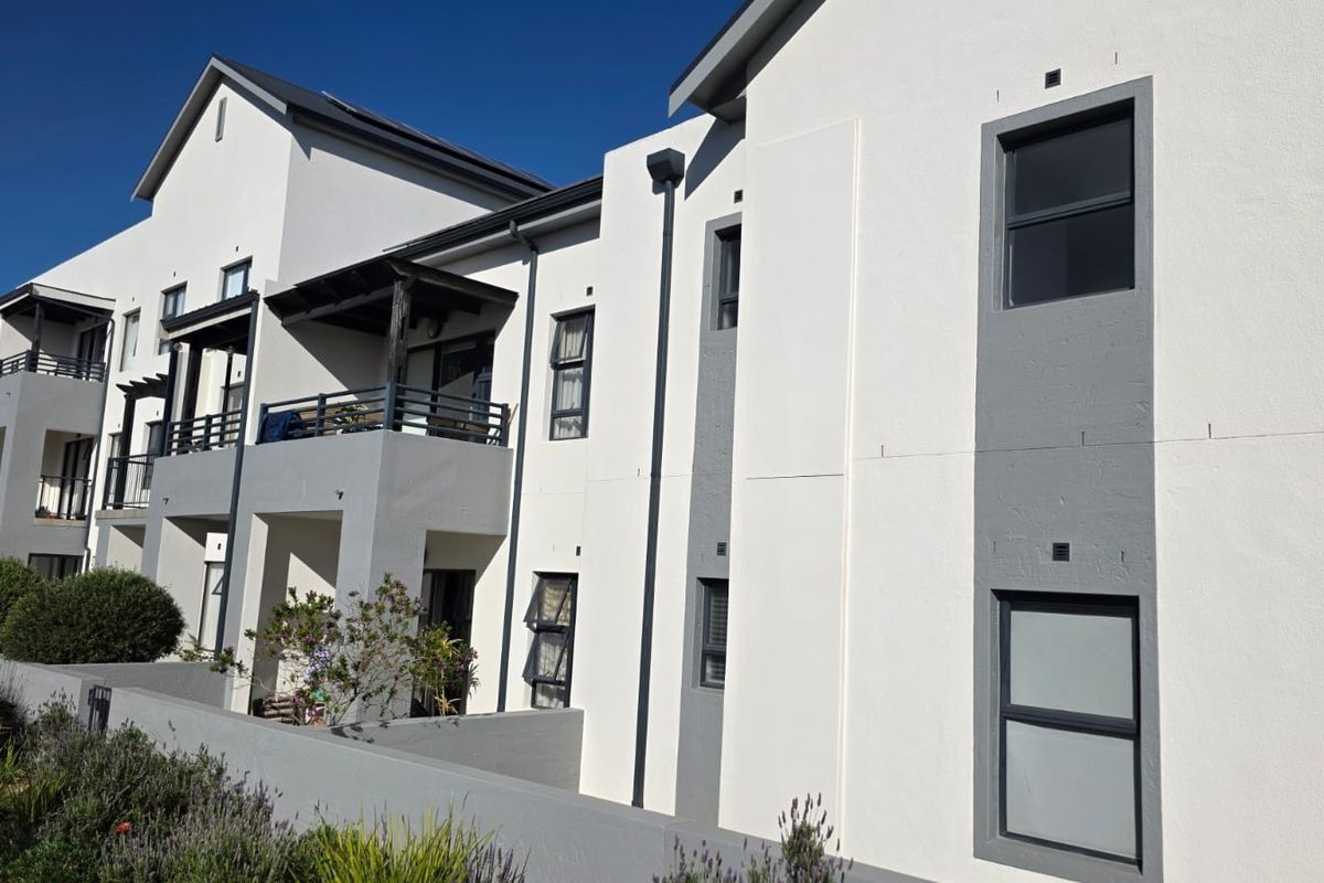 A modern multi-story residential building featuring clean white and grey facade finishes, private balconies, and well-maintained landscaped garden areas.