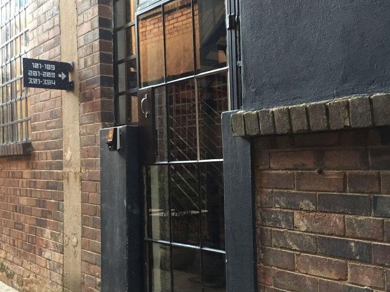 Industrial-style entrance featuring a steel-framed glass door set within an exposed brick facade, complete with directional signage and an intercom system.