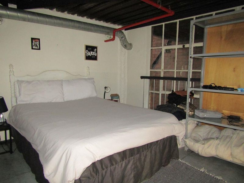 Bedroom featuring industrial-style exposed ducting, piping, and large window, offering a raw, urban aesthetic suitable for modern renovation.