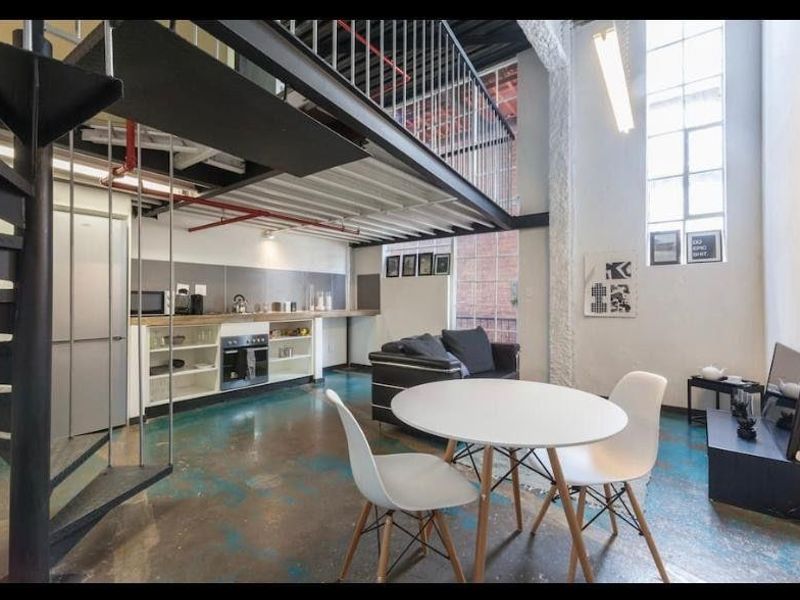 Spacious industrial-style open plan apartment featuring a mezzanine level, spiral staircase, polished concrete floors, and large windows providing ample natural light.