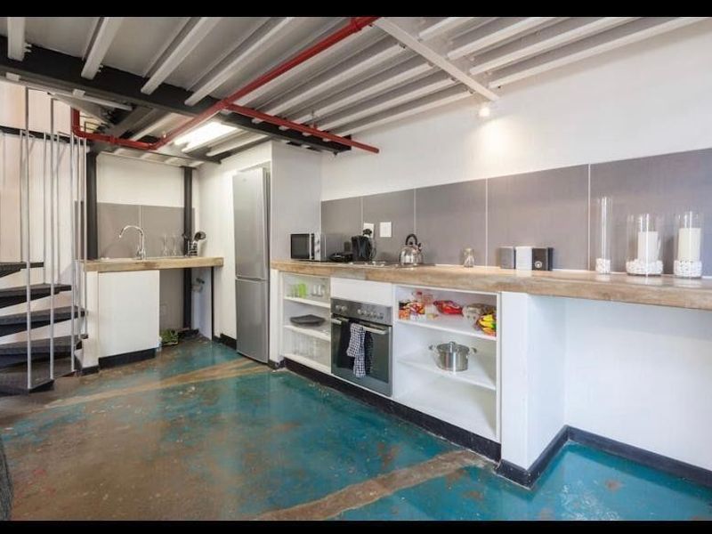 Industrial-style kitchen featuring exposed ceiling beams, a spiral staircase, built-in oven, and concrete flooring with a functional layout.