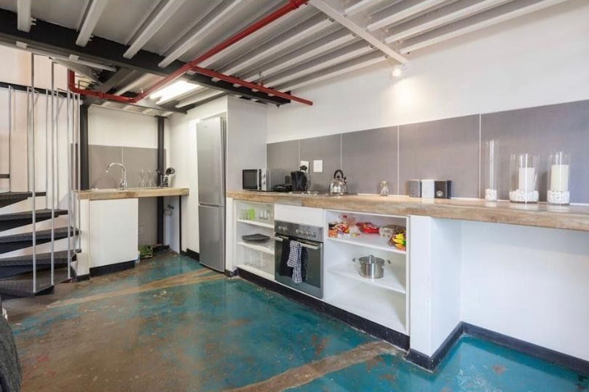 Industrial-style kitchen featuring exposed ceiling beams, a spiral staircase, built-in oven, and concrete flooring with a functional layout.