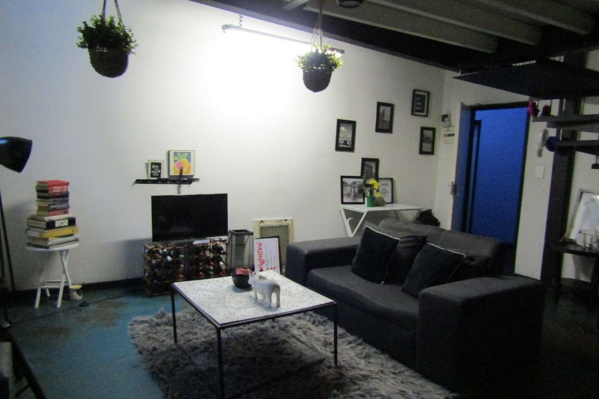 Living room featuring industrial-style exposed steel ceiling beams and painted concrete flooring, offering a versatile space for personalization.