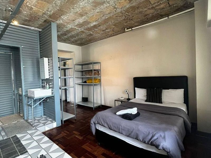A unique bedroom featuring an exposed brick vaulted ceiling, rich parquet flooring, and an integrated washbasin area with industrial-style exposed plumbing.