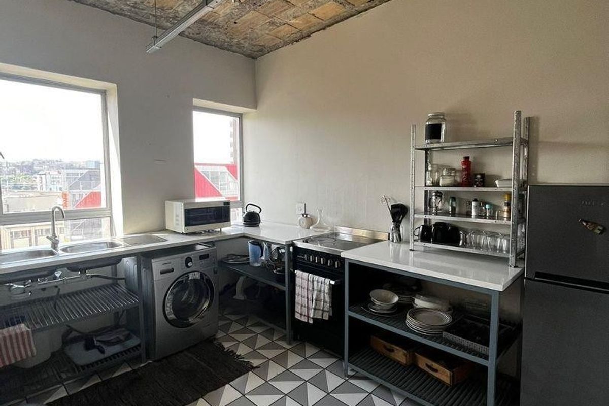 Industrial-style kitchen featuring an exposed brick ceiling, patterned tiled flooring, stainless steel sink, and built-in oven with ample counter space.