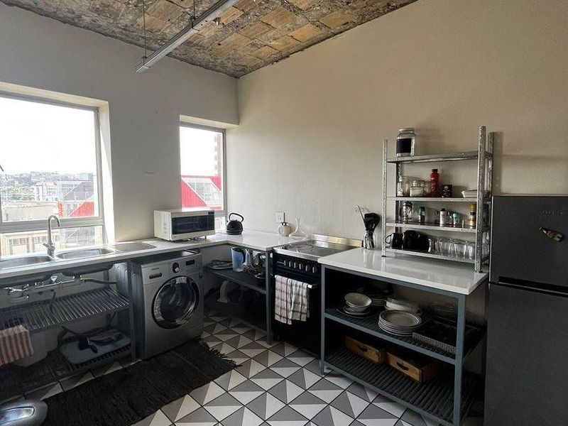 Industrial-style kitchen featuring an exposed brick ceiling, patterned tiled flooring, stainless steel sink, and built-in oven with ample counter space.
