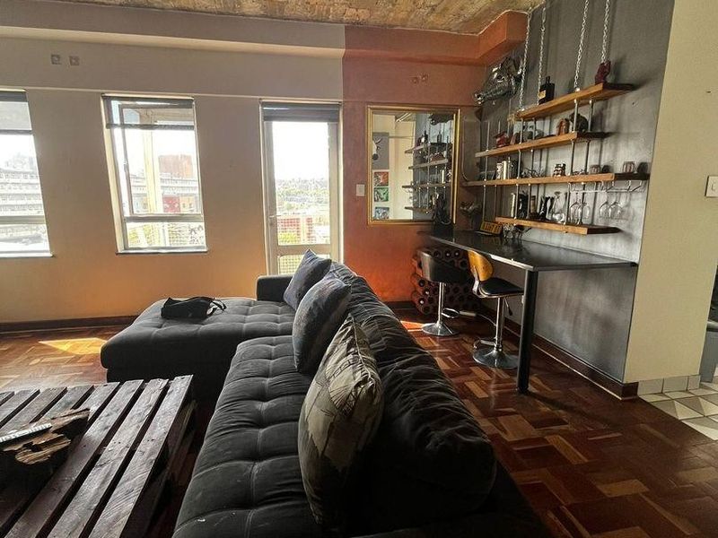 Living room featuring an industrial aesthetic with an exposed brick ceiling, parquet flooring, and a built-in bar area with wall-mounted shelving.