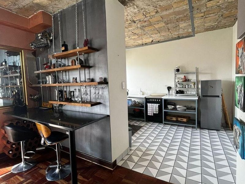 Open plan kitchen and dining area featuring industrial-style exposed brick ceilings, a mix of parquet and geometric tile flooring, and a built-in breakfast bar.