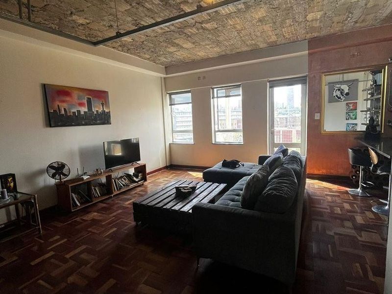 Spacious living area featuring unique exposed brick ceilings, warm parquet flooring, and industrial-style track lighting, creating a character-filled urban apartment space.