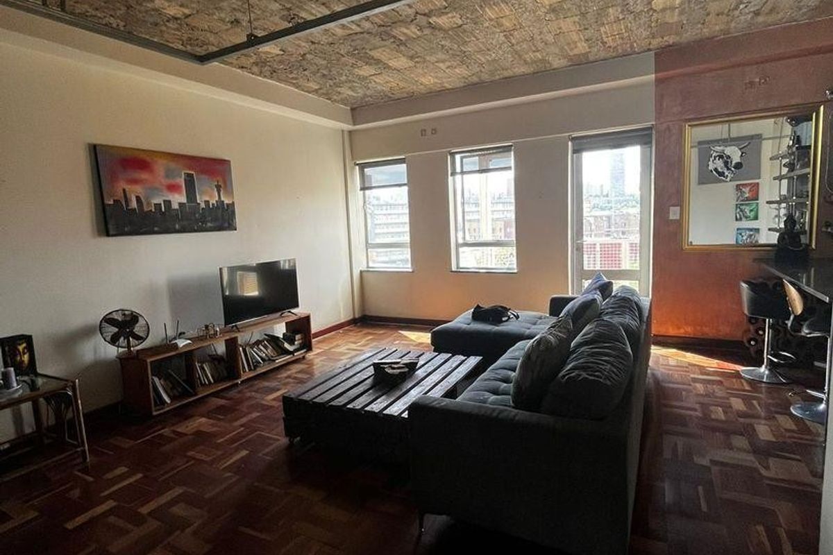 Spacious living area featuring unique exposed brick ceilings, warm parquet flooring, and industrial-style track lighting, creating a character-filled urban apartment space.