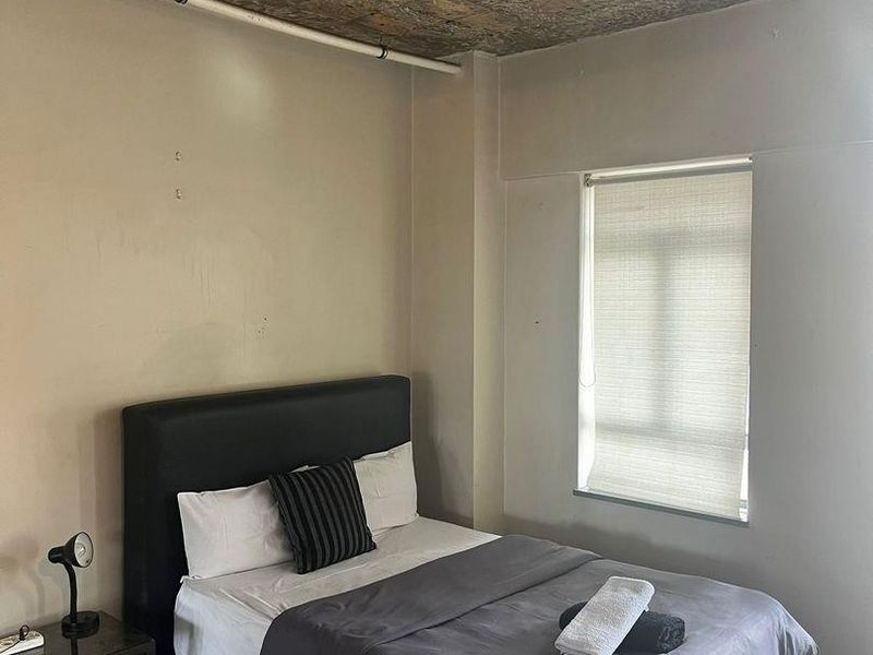 A bedroom featuring parquet flooring and an industrial-style exposed concrete block ceiling with a roller blind on the window.