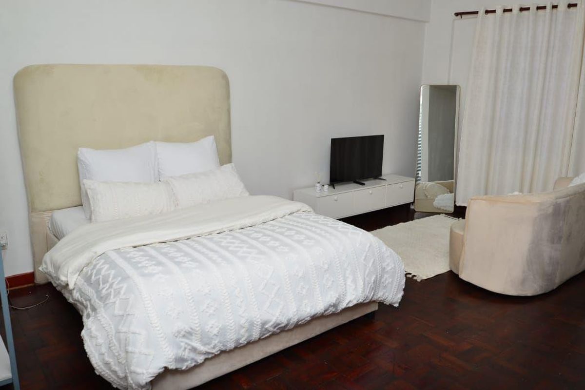 A well-lit bedroom featuring dark parquet flooring and neutral wall finishes, providing a comfortable and functional living space.