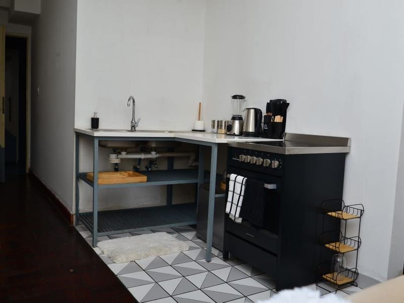 Compact kitchen area featuring a stainless steel sink, open shelving, and a modern black freestanding stove with patterned floor tiles.
