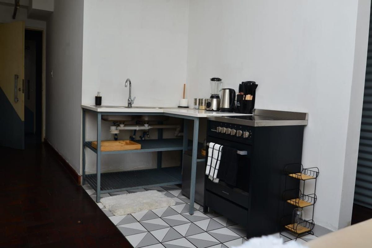 Compact kitchen area featuring a stainless steel sink, open shelving, and a modern black freestanding stove with patterned floor tiles.