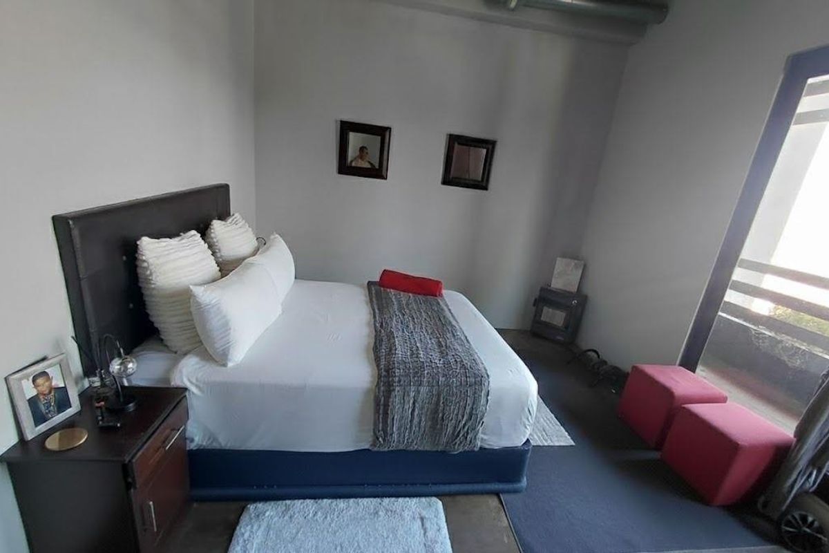 A bedroom featuring neutral walls, exposed ceiling ducting, and a large sliding glass door providing access to an outdoor area.