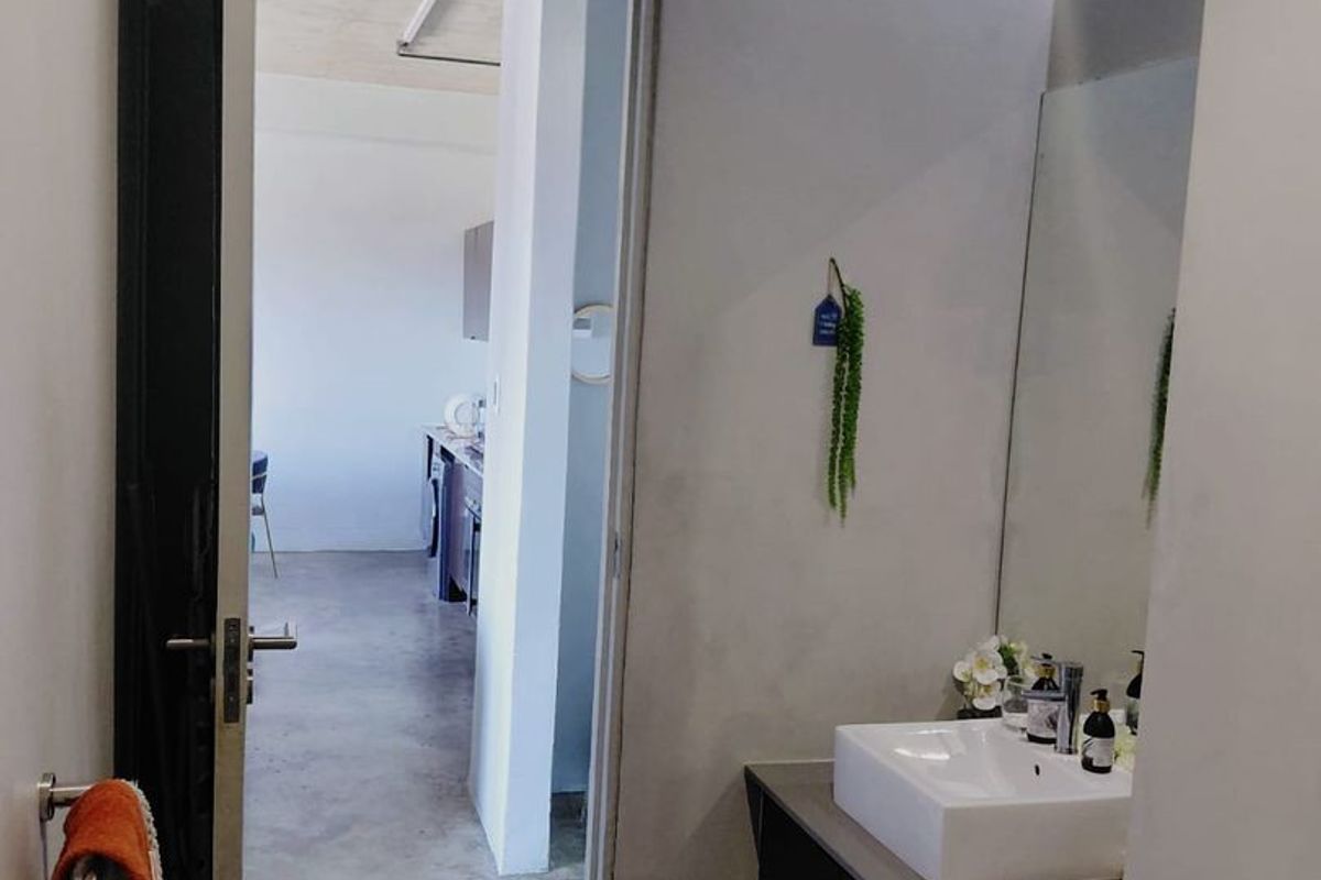 A modern bathroom featuring a sleek vanity with a countertop basin, wall-mounted mirror, and polished concrete flooring, with a view into the adjacent living area.