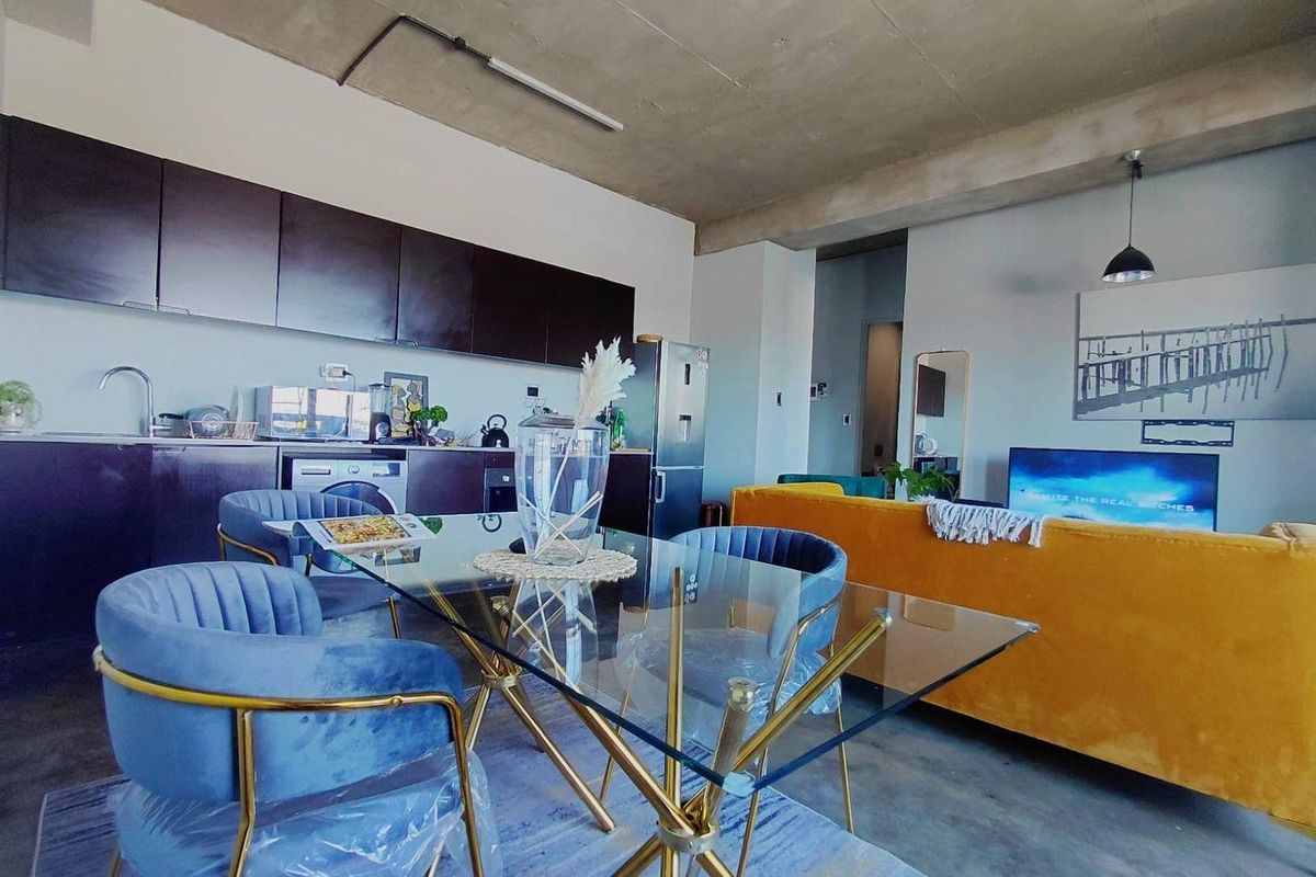 Modern open-plan living area featuring an industrial-style exposed concrete ceiling, polished concrete floors, and a sleek kitchen with dark cabinetry and integrated appliances.