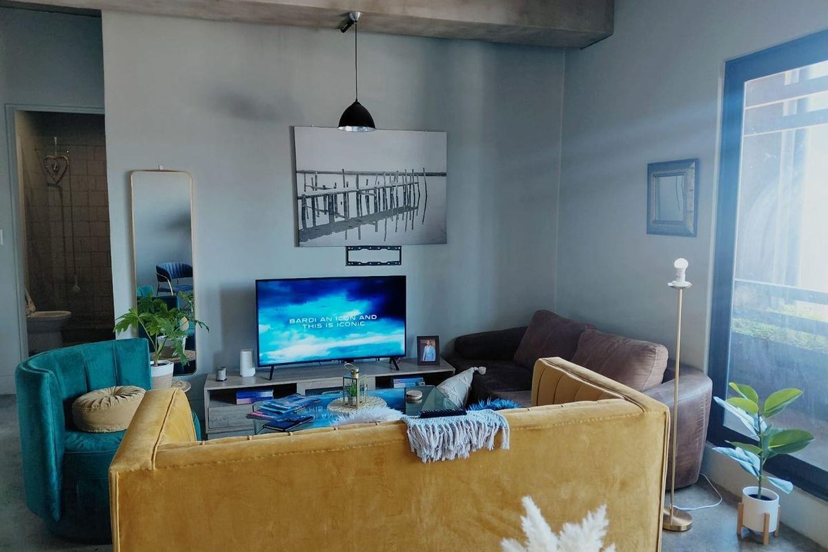 A contemporary living room featuring polished concrete floors, an exposed concrete ceiling beam, and large sliding glass doors providing natural light.