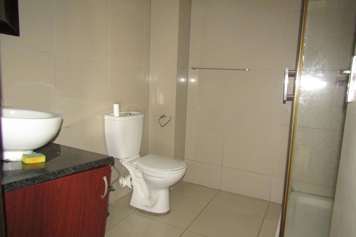 A functional bathroom featuring a vanity with a vessel sink, a toilet, and a glass-enclosed shower with neutral wall and floor tiling.