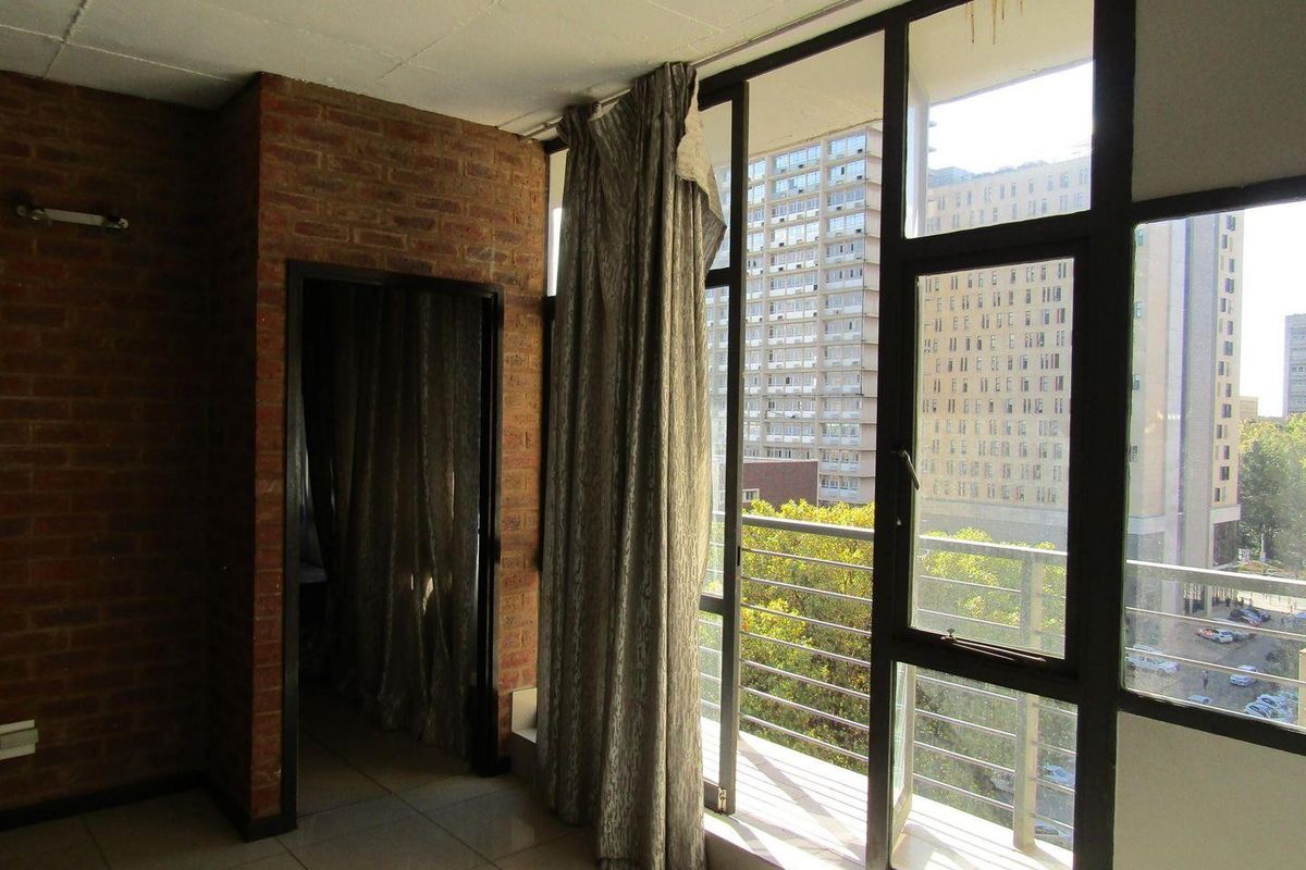 Living area featuring exposed brick walls, large windows with balcony access, and tiled flooring, offering an urban view.
