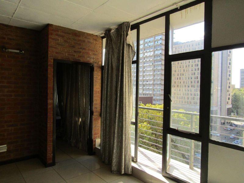 Living area featuring exposed brick walls, large windows with balcony access, and tiled flooring, offering an urban view.
