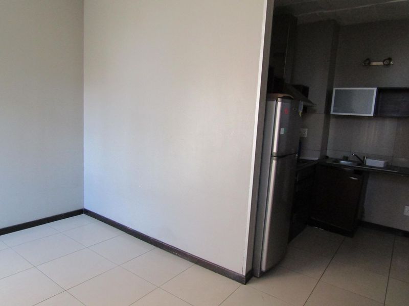 An open-plan living area featuring tiled flooring and an adjacent compact kitchen with built-in cabinetry and sink.