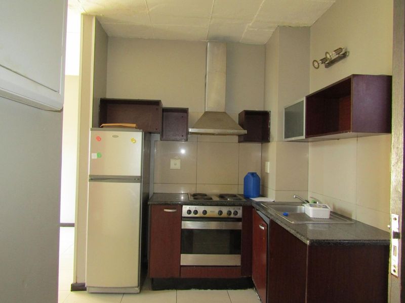Compact kitchen featuring dark wood cabinetry, granite countertops, built-in oven, and stainless steel extractor fan, requiring some cosmetic updates to cabinetry and ceiling.
