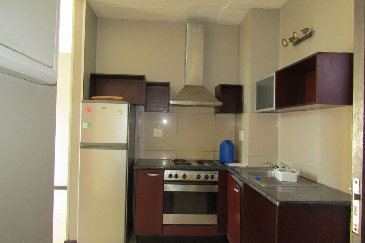Compact kitchen featuring dark wood cabinetry, granite countertops, built-in oven, and stainless steel extractor fan, requiring some cosmetic updates to cabinetry and ceiling.