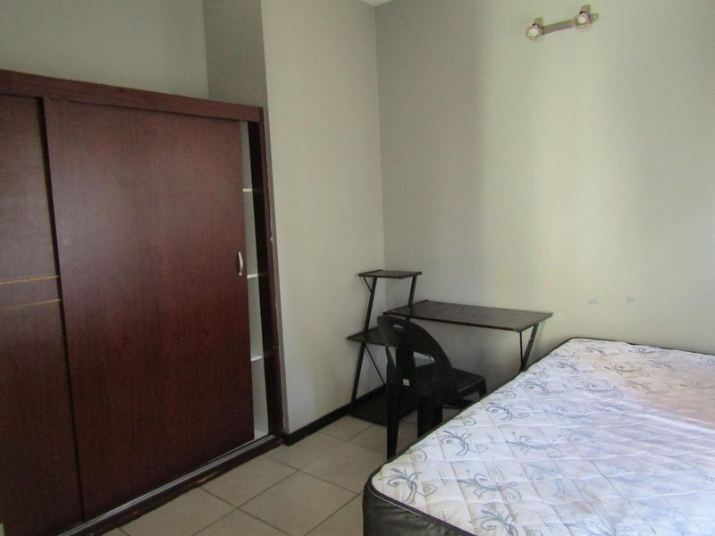 A functional bedroom featuring tiled flooring, a built-in sliding door wardrobe, and a wall-mounted light fixture.