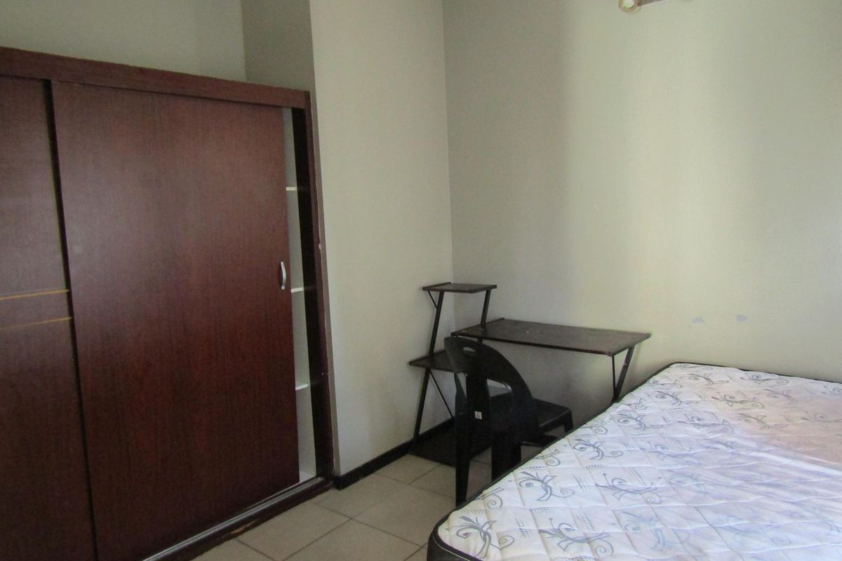 A functional bedroom featuring tiled flooring, a built-in sliding door wardrobe, and a wall-mounted light fixture.