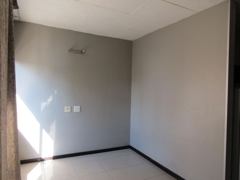 A clean, empty bedroom featuring neutral grey walls, tiled flooring, and basic electrical fixtures, providing a blank canvas for personalization.