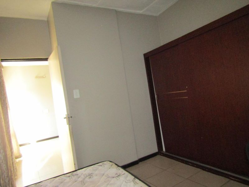 A bedroom featuring tiled flooring and a built-in wooden wardrobe, offering a functional space ready for personalization.