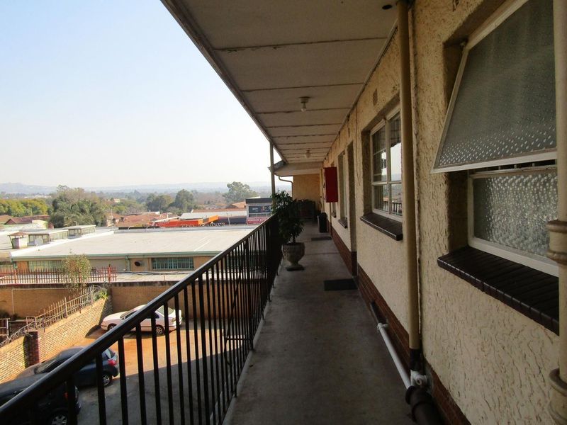An exterior balcony walkway featuring a metal balustrade, concrete flooring, and views over the surrounding neighbourhood.