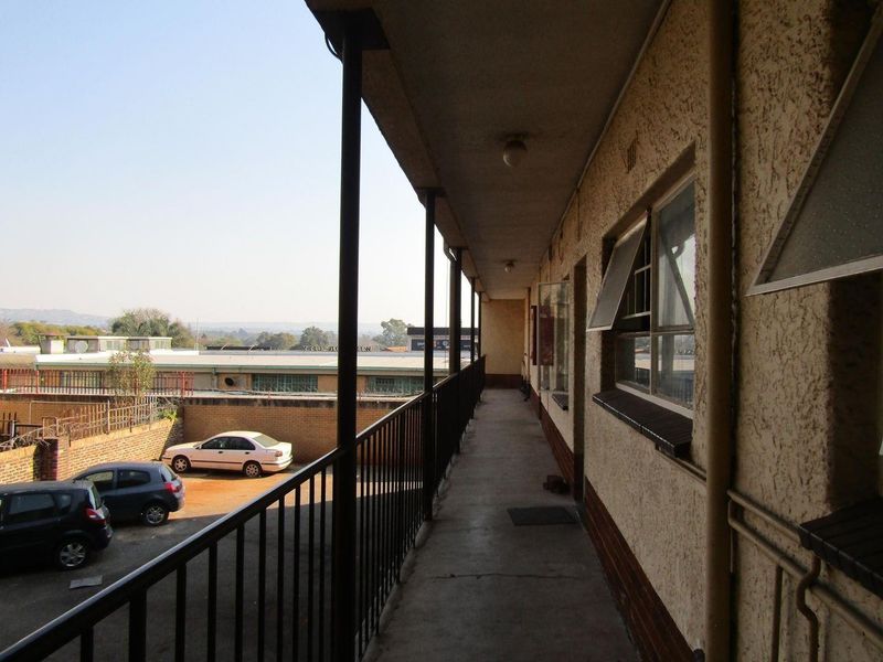 An exterior apartment balcony walkway featuring metal railings and views over the parking area and surrounding neighborhood.