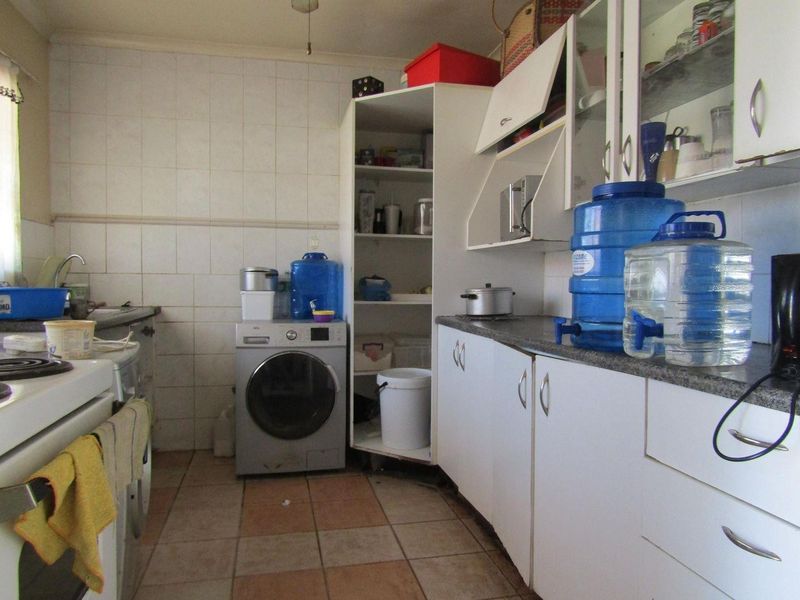 A functional kitchen featuring built-in cabinetry, tiled splashbacks, and integrated appliances, currently showing signs of wear and dated finishes.