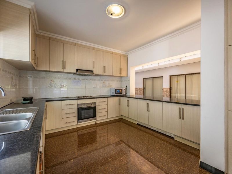 A spacious kitchen featuring light wood cabinetry, granite countertops, built-in oven, gas hob, and polished tiled flooring.