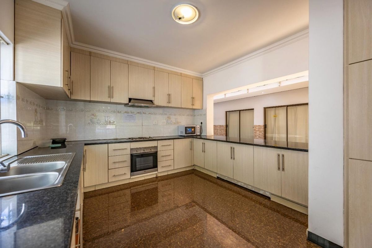 A spacious kitchen featuring light wood cabinetry, granite countertops, built-in oven, gas hob, and polished tiled flooring.