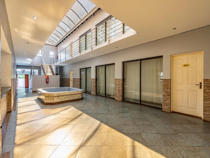Spacious indoor atrium or hallway featuring tiled flooring, a large skylight, stainless steel balustrades, and multiple access points to adjacent rooms.